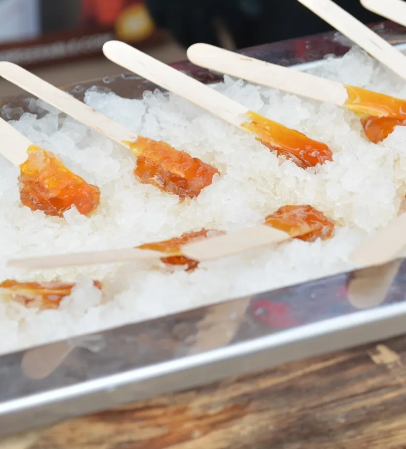 Photo de bâtonnets de tire d’érable reposant dans un contenant rempli de neige.