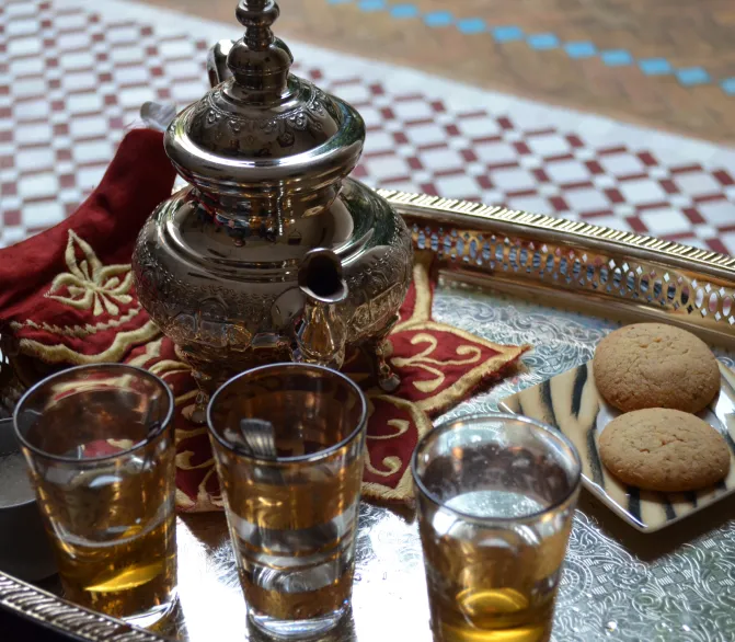 Photo d’un plateau en métal contenant une théière, trois petits verres de thé et deux biscuits.