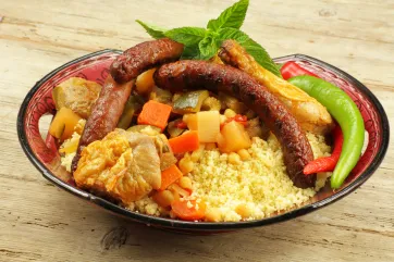 Photo d’une assiette creuse remplie de couscous, de saucisses et de différents légumes.
