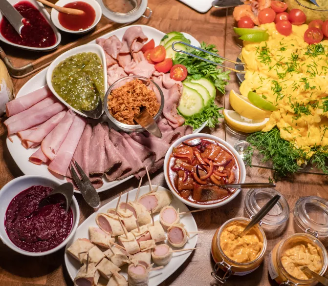 Photo d’un ensemble de plusieurs plats, entre autres une omelette, des charcuteries, des bouts de saucisses enroulés, des crudités, des sauces.